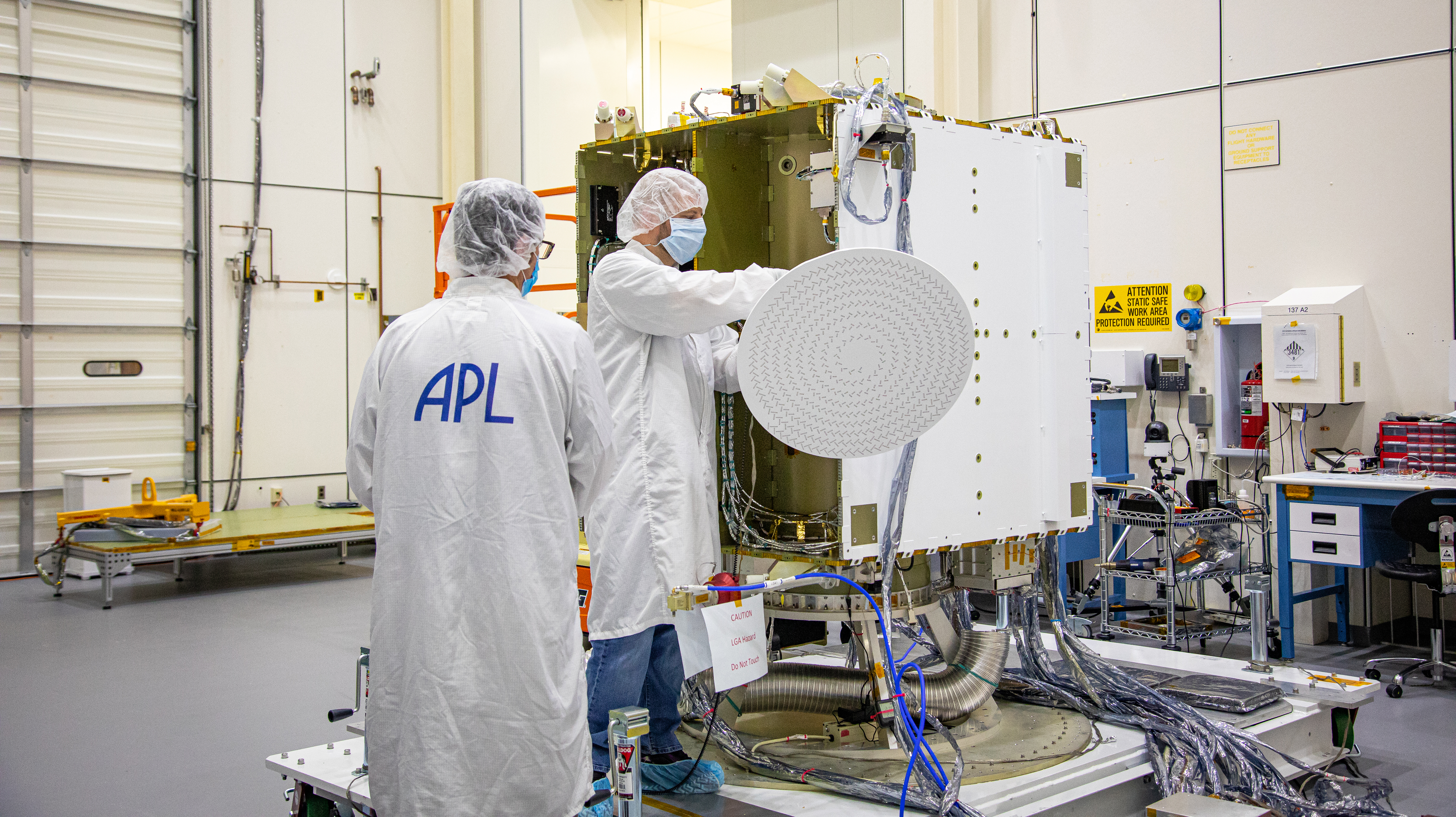 Two people in personal protective gear work on a part of the DART spacecraft