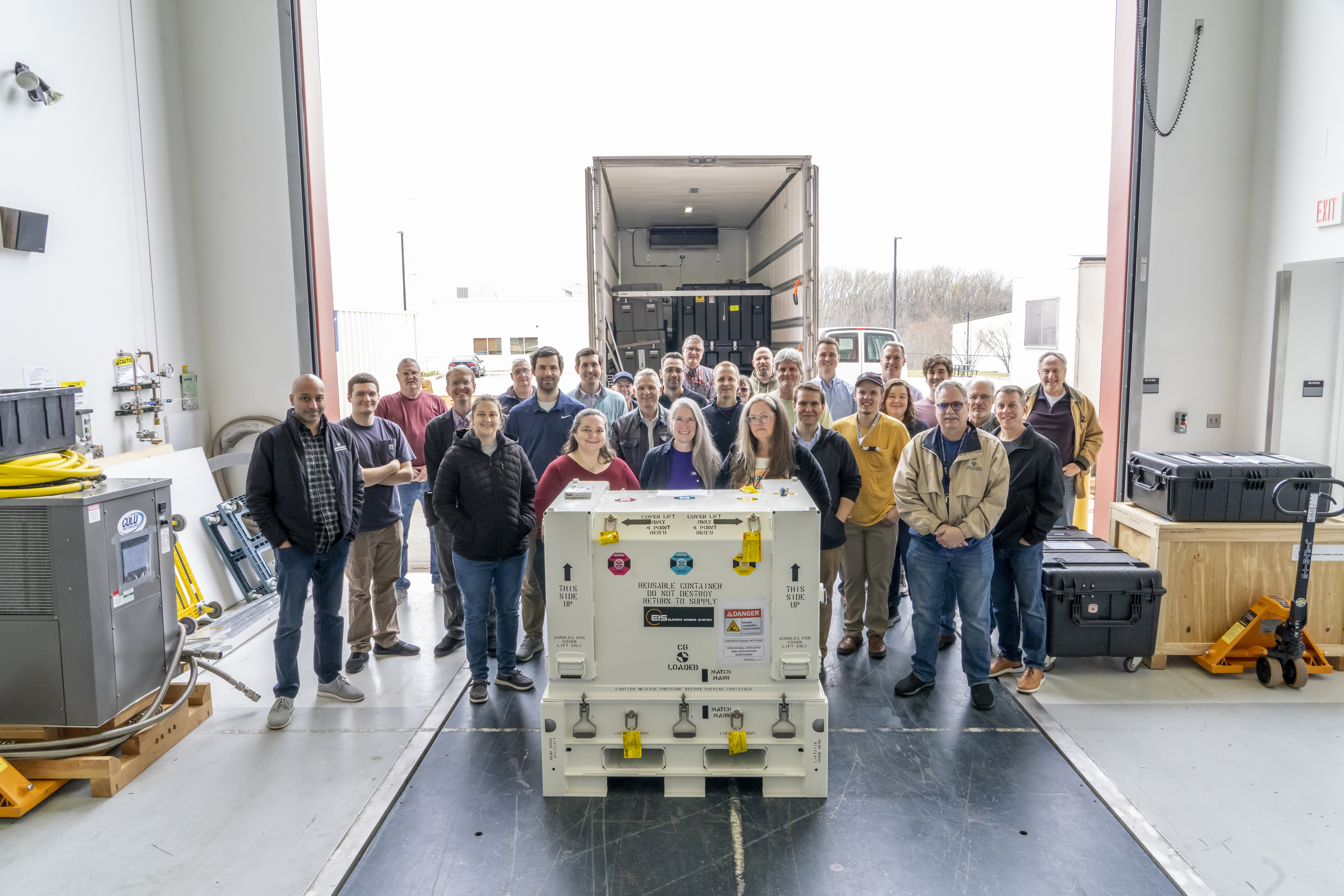 A group of people stand in front of the open doors of a FedEx truck and behind a closed white temperature-sensitive box that's holding the EIS NAC instrument
