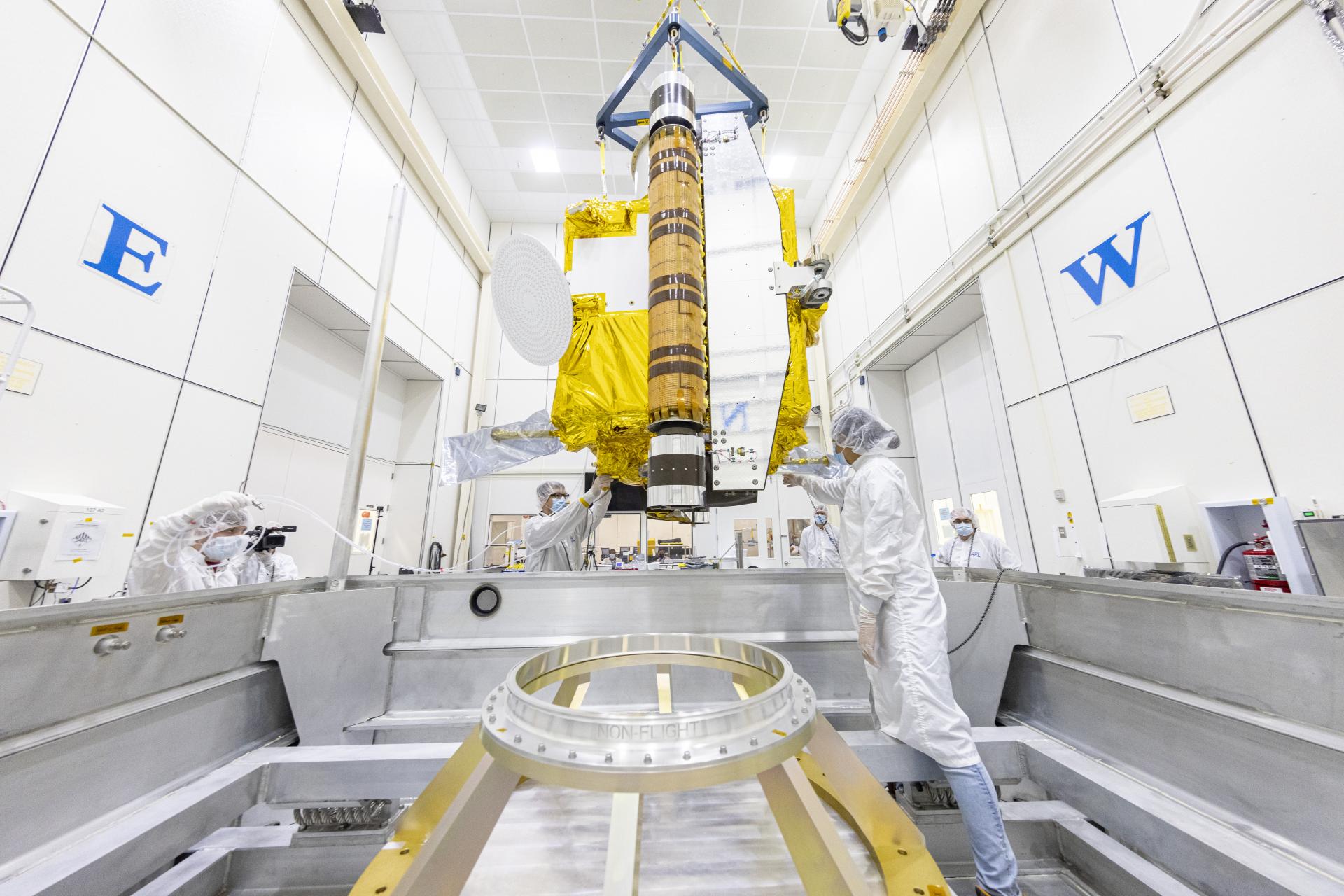 Image of people moving the dangling DART spacecraft into its specialized container