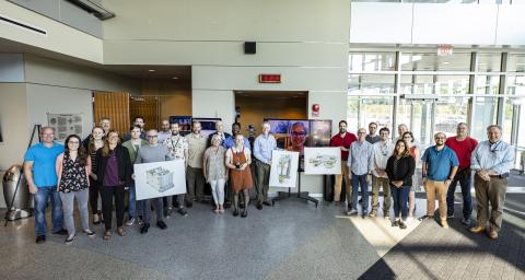 A group of people stands with a few holding images of spacecraft instruments