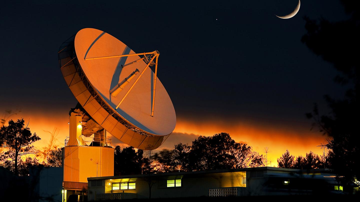 APL's large satellite dish aglow in orange light under the moon